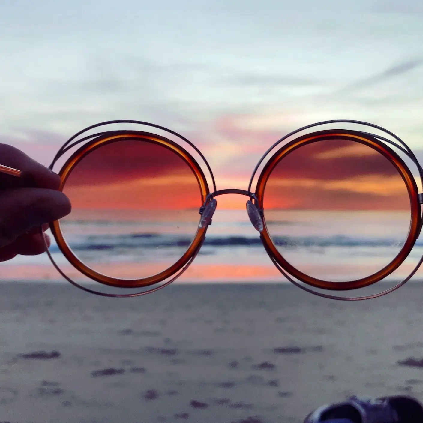 a person holding up a pair of sunglasses on the beach